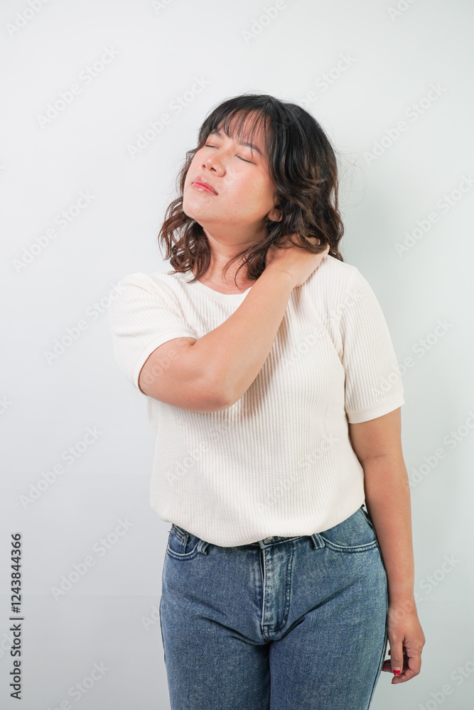 Beautiful young asian woman with wavy hair wearing white shirt is suffering from neck and shoulder muscle pain with grimacing face expression, isolated over white background. Beautiful young asian woman with wavy hair wearing white shirt is suffering from neck and shoulder muscle pain with grimacing face expression, isolated over white background.