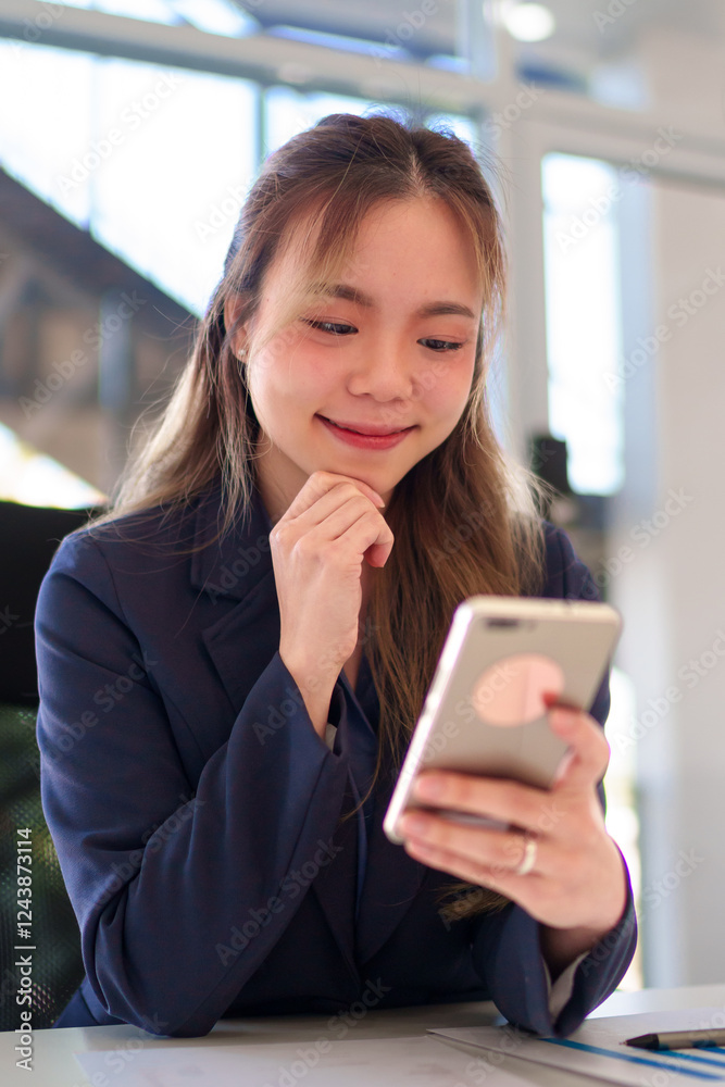 Close-up of a young Asian businesswoman using a smartphone while working in a bright and modern office Close-up of a young Asian businesswoman using a smartphone while working in a bright and modern office