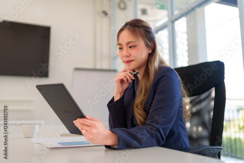 Close-up of a young Asian businesswoman holding a tablet and gesturing while discussing business data in a modern office