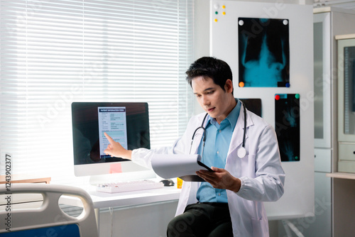 Young doctor pointing at patient information form on computer screen while holding medical records in hospital room