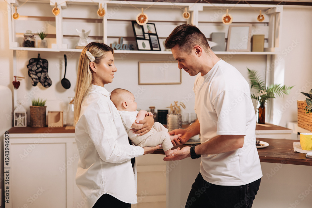 Fototapeta premium Happy family with newborn son playing in the kitchen. Family couple at home with son making coffee in the kitchen. Home family atmosphere