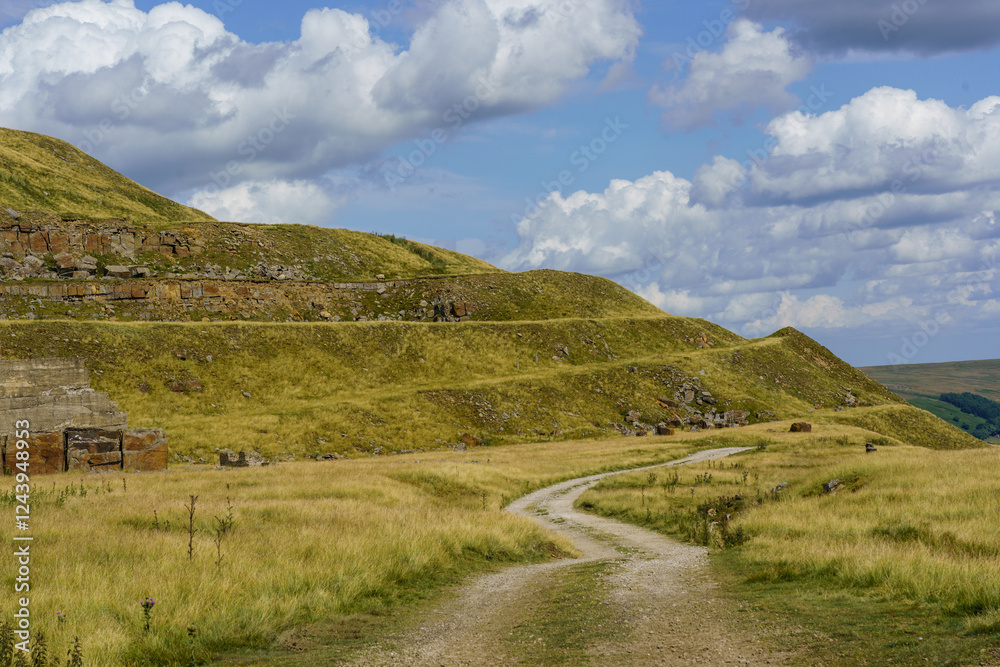 A winding dirt path meanders across a field towards rolling hills and the remnants of a quarry, Scar House Reservoir, North Yorkshire, UK. A winding dirt path meanders across a field towards rolling hills and the remnants of a quarry, Scar House Reservoir, North Yorkshire, UK.