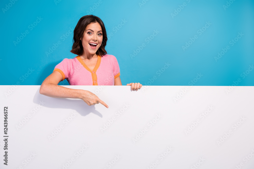 Smiling young woman pointing at blank panel with blue background emphasizing cheerful and vibrant concept Smiling young woman pointing at blank panel with blue background emphasizing cheerful and vibrant concept