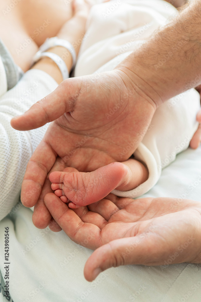 Father's hands holding tiny newborn baby's foot in hospital Father's hands holding tiny newborn baby's foot in hospital