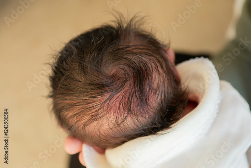 Close-up of newborn baby's head with dark brown hair and cowlick in hospital photo