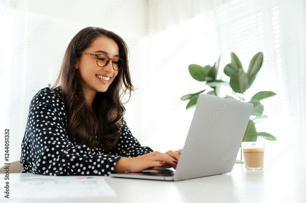 Happy charming brunette caucasian or arabian woman, office secretary, sits at a white desk with a laptop surrounded by documents, maintains correspondence with clients or colleagues, smile friendly Happy charming brunette caucasian or arabian woman, office secretary, sits at a white desk with a laptop surrounded by documents, maintains correspondence with clients or colleagues, smile friendly