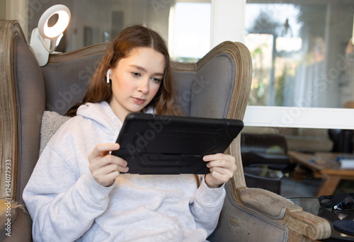 Teenage girl sitting at home on an armchair with iPad