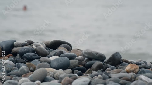 A beautiful, calm beach scene is depicted with smooth stones lining the shore where gentle waves lap softly