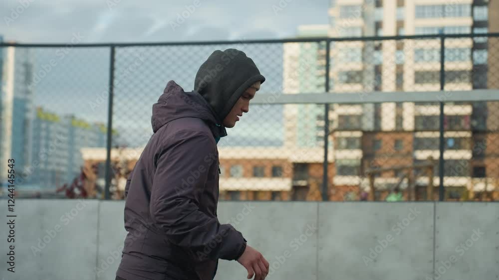 Man practicing in sport arena looking visibly tired, preparing near goalpost, background features urban residential buildings and mesh fence Man practicing in sport arena looking visibly tired, preparing near goalpost, background features urban residential buildings and mesh fence