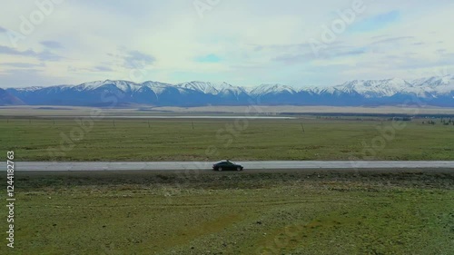 Car drives out onto a road in a mountainous valley. A quadcopter follows the car.