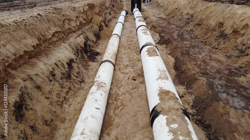 Two pipes are laying in the dirt, one of which is covered in mud. The other pipe is covered in dirt and mud