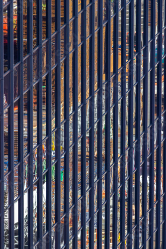 Obraz na płótnie A close-up view of a modern building's facade, showcasing vertical metal bars with reflections of a vibrant cityscape, creating an abstract and dynamic visual effect. w salonie