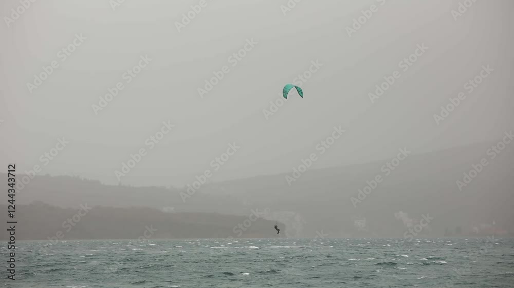 Extreme kiteboarding in stormy weather in the bay of the sea in Italy. Surfer in a black wetsuit jump with kite. Slow motion Extreme kiteboarding in stormy weather in the bay of the sea in Italy. Surfer in a black wetsuit jump with kite. Slow motion