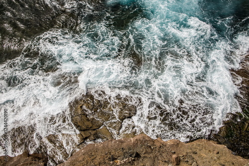 Obraz na płótnie Aerial view of waves crashing against rocks on a shoreline. Dynamic patterns and textures in the water and rocks. w salonie
