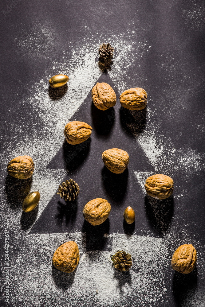 Creative Christmas flat lay with nuts, pinecones, and gold decorations arranged in a tree shape on a dark
