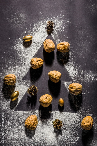 Obraz na płótnie Creative Christmas flat lay with nuts, pinecones, and gold decorations arranged in a tree shape on a dark w salonie