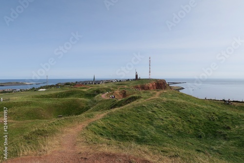 Vom Hügel Pinneberg auf dem Oberland ist ein Landschaftspanorama der Insel Helgoland zu sehen. Auffällig sind der Leuchtturm, ein Funkmast, die roten Klippen, die Nordsee und die Nachbarinsel Düne.