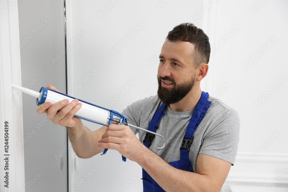 Worker with caulking gun sealing window indoors Worker with caulking gun sealing window indoors