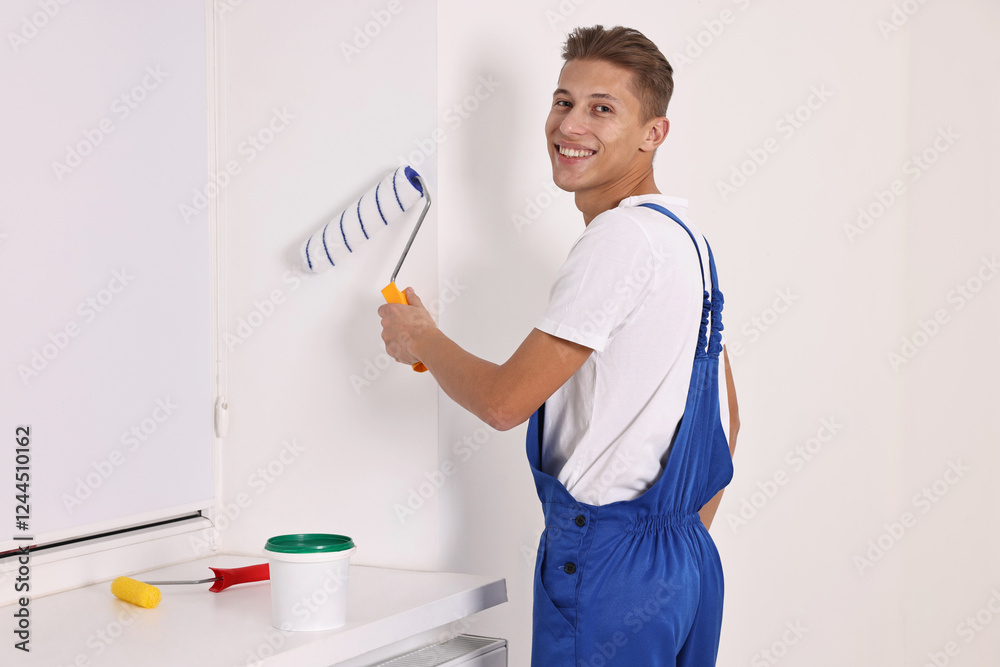 Smiling handyman painting wall with roller indoors Smiling handyman painting wall with roller indoors