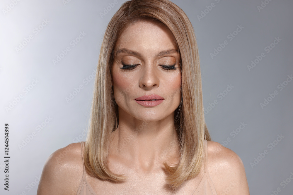 Fototapeta premium Portrait of beautiful woman with straight blonde hair and stylish makeup on light grey background