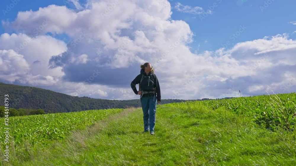 Standing backpacking hiker taking in the lush farmland and grassy meadow before continuing to walk on a partly cloudy summer day, Rhine Valley, Germany Standing backpacking hiker taking in the lush farmland and grassy meadow before continuing to walk on a partly cloudy summer day, Rhine Valley, Germany