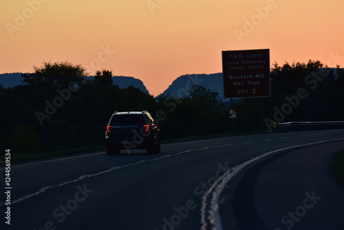 Sunset over an American highway with a road sign and a vehicle. Scenic view, road trip, travel, journey, American landscape, highway, sunset glow, evening drive, adventure, freedom on the road