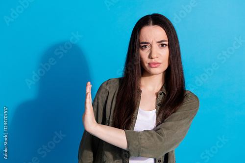 Tableau sur toile Confident young woman gesturing stop with hand against a vivid blue backdrop, ex