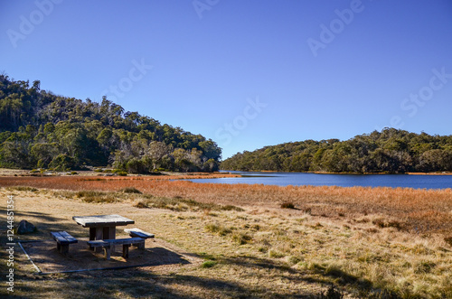 Lake Catani nestled within the majestic Mount Buffalo National Park, Australia. A solitary picnic table and benches overlooking the tranquil lake and lush, forested slopes of the surrounding mountains photo