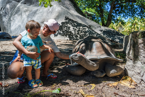 Asian mother with child playing with a giant tortoise, La Digue island, Seychelles photo