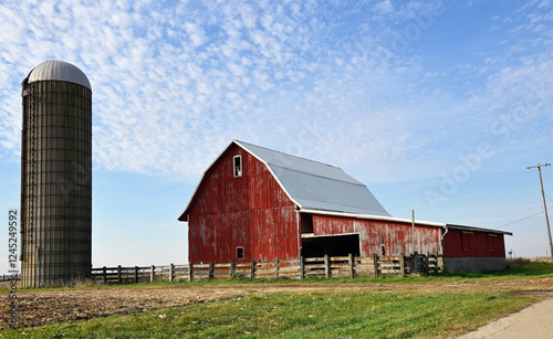 A weathered red barn sits along a country road in the Midwestern United States. The image depicts what is often an isolated lifestyle.