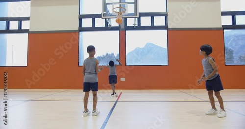 Playing basketball in school gym, three boys practicing dribbling and passing