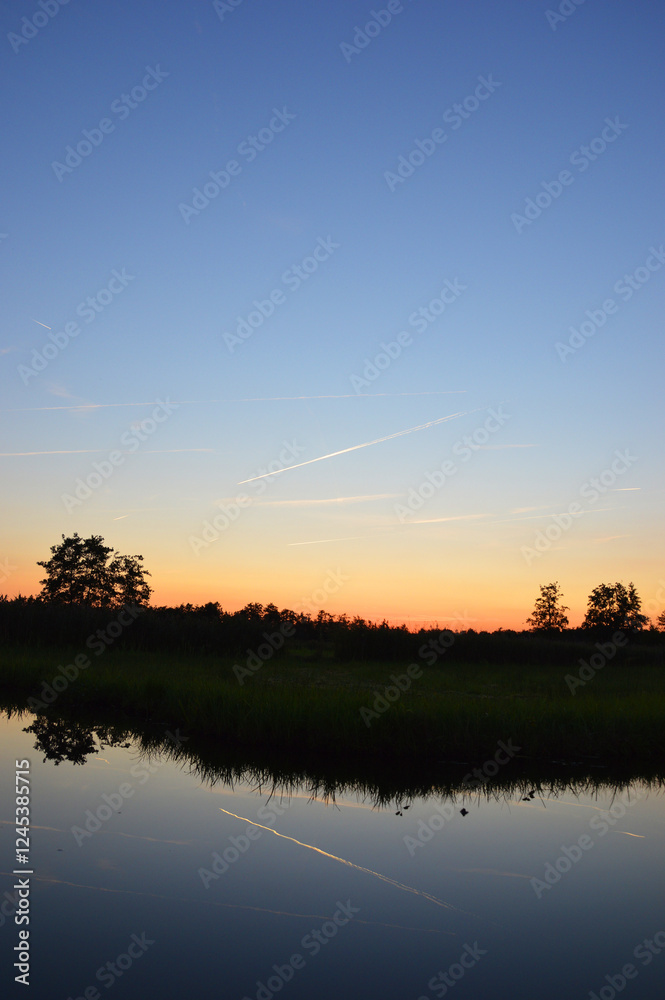Fototapeta premium Beautiful view of sunset sky above reflected on calm river below