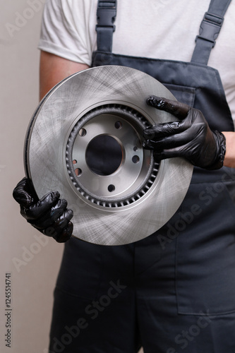 Auto mechanic holding new brake disc in hands in black gloves, close-up. Auto parts replacement concept, serviceable car brake system. Vertical
