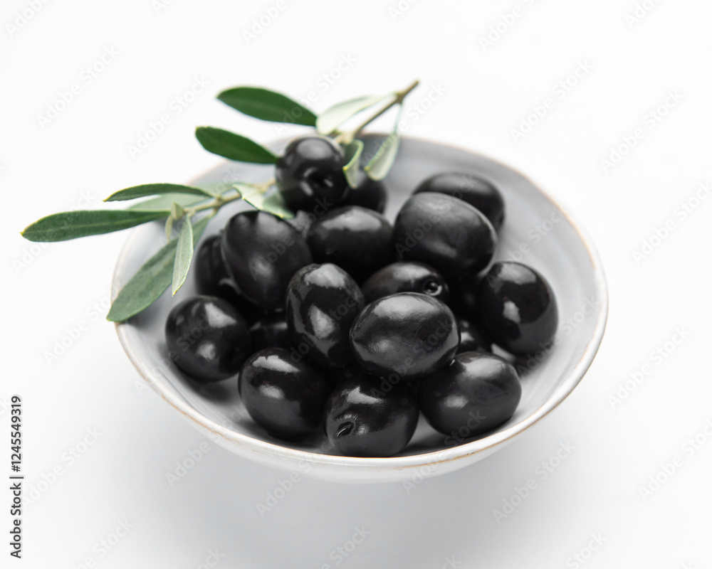 Black olives with leaves in a bowl on white background