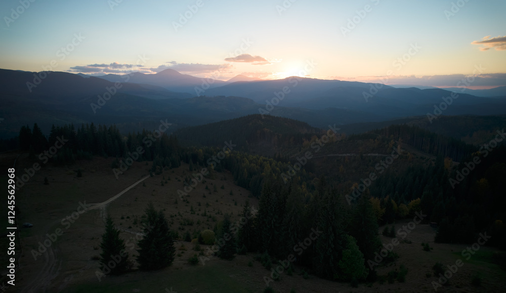 Obraz premium Aerial view of verdant mountain landscape bathed in morning light. Rolling hills with scattered farmhouses interspersed with patches of forest. Sunlight creates long shadows.