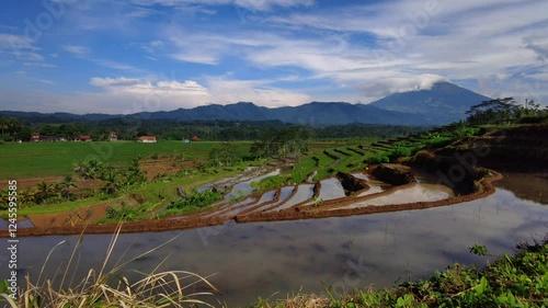 The beauty of neatly arranged rice field terraces, shadows of clumps and trees in the morning, with some farmers who are resting, with a beautiful mountain background and blue sky