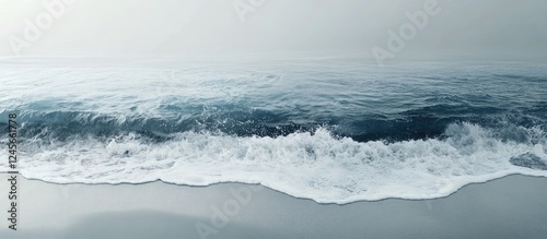 Serene coastal scene featuring gentle waves crashing onto a smooth gray white sandy beach under a calm blue ocean sky in a panoramic view