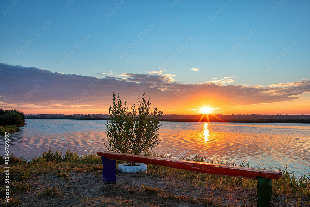 Majestic sunset over tranquil waters with a colorful bench in a serene landscape