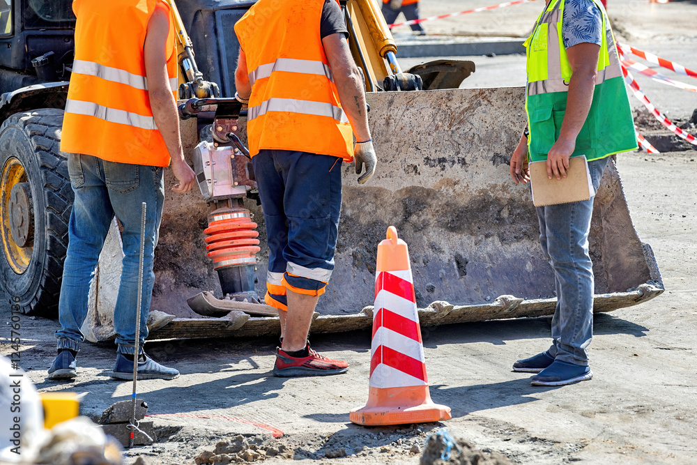 Workers in bright vests operate machinery at a construction site under the sun