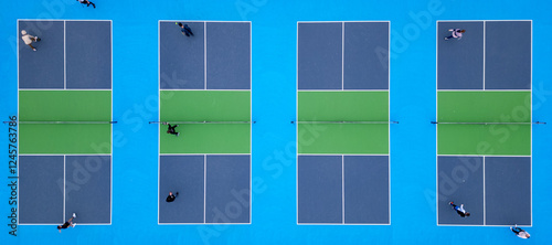 Aerial top-down view of multiple pickleball courts with players engaged in a match. The vibrant blue and green surfaces create a striking geometric pattern, capturing the dynamic movement and energy