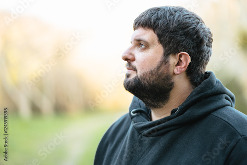 Deaf man using hearing aid outdoors in natural surroundings during a calm day