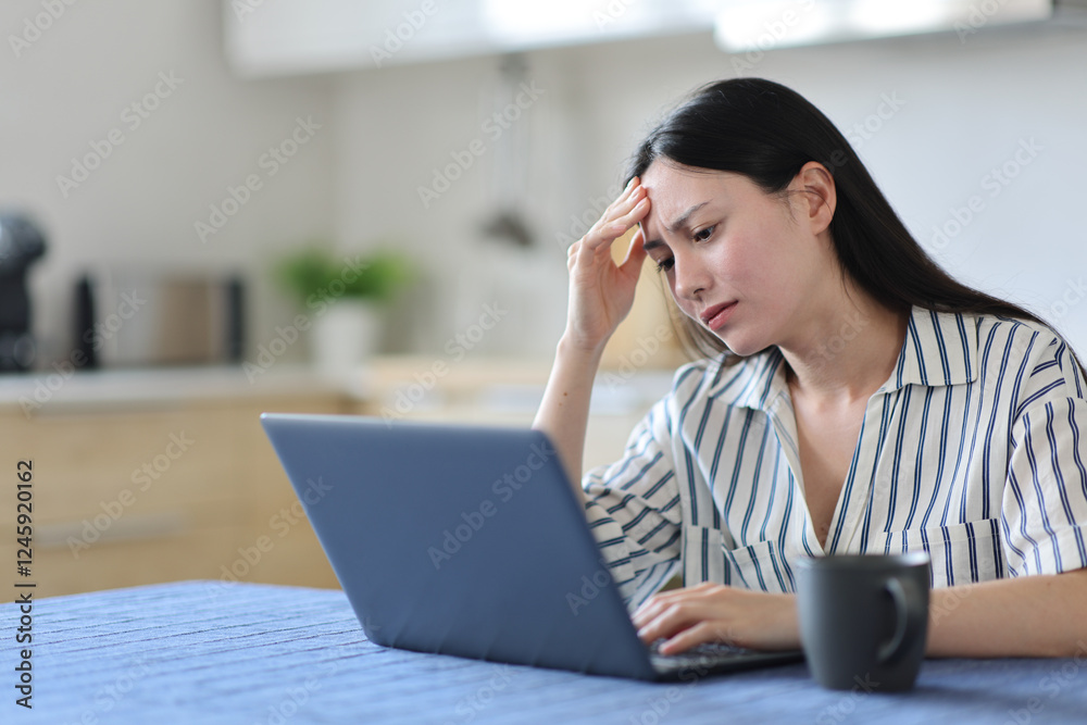 Worried asian woman checking laptop in the kitchen Worried asian woman checking laptop in the kitchen