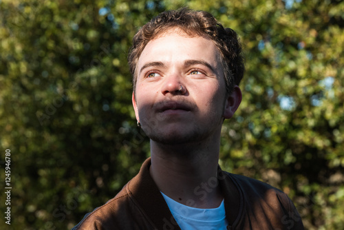 Trans man enjoys sunlight in a park surrounded by greenery on a clear day