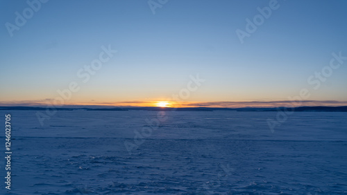 Frozen Horizon Under Winter Dawn - The sun rises over the frozen expanse of Khovsgol lake, casting a soft golden hue across the icy landscape. photo