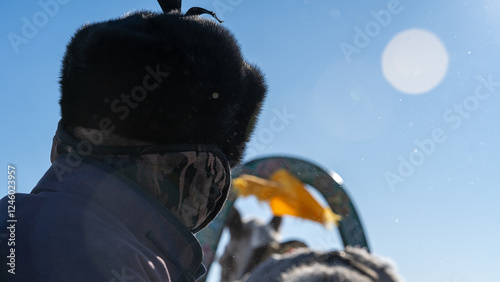 Winter Rider Under Arctic Sky - A person wearing fur-lined winter clothing rides a traditional sled, with the blue sky and frosty air surrounding them. photo