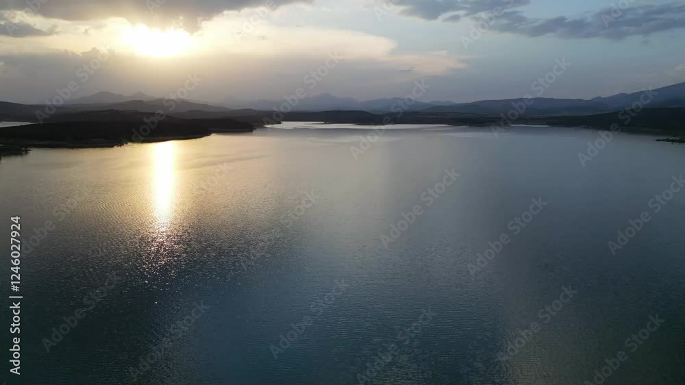 Golden sunset reflecting on calm lake water with mountains in background Golden sunset reflecting on calm lake water with mountains in background