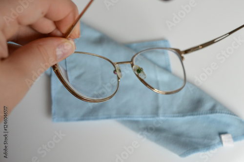 hand cleaning eyeglasses with a soft microfiber cloth golden-rimmed glasses wiped importance lens care hygiene maintenance eyewear optometry vision health tips minimalist stores 