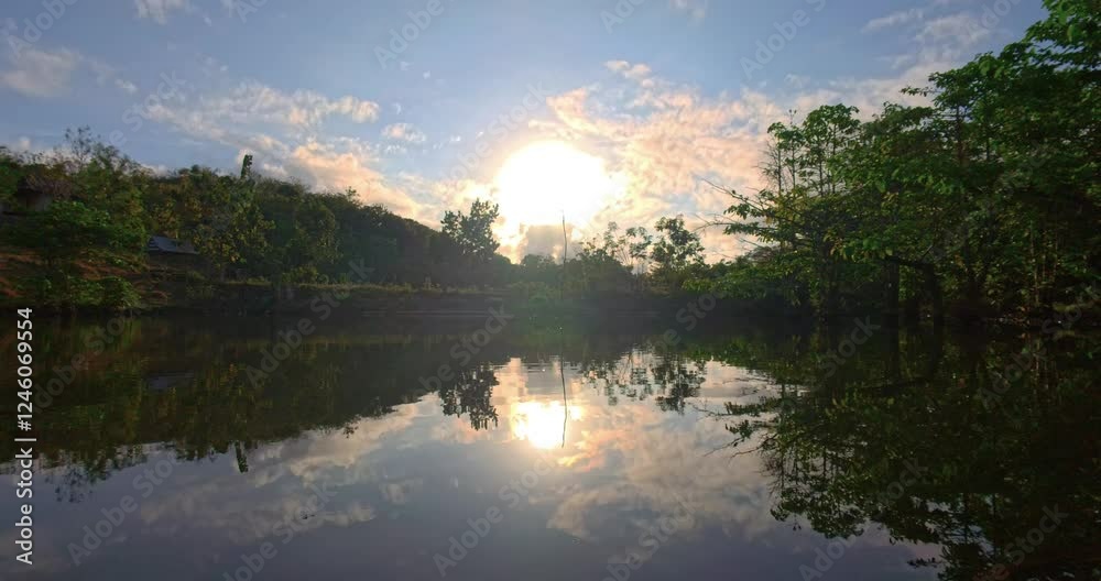 A serene sunrise over a calm lake, showcasing vibrant colors reflecting on the water's surface. The angle highlights the lush greenery surrounding the lake, creating a peaceful atmosphere