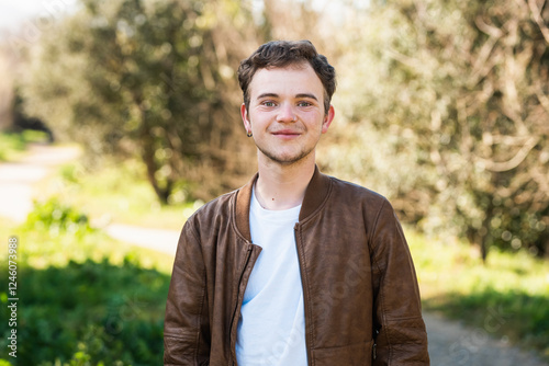 Transgender man enjoying a sunny afternoon in a green outdoor setting with trees and a pathway