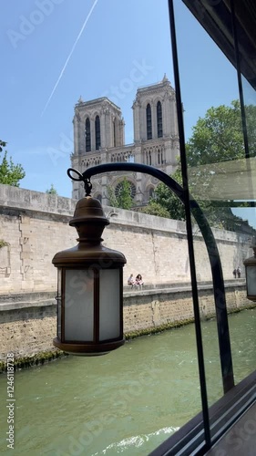 A scenic view of Notre-Dame Cathedral in Paris, seen through a window with a vintage lantern, overlooking the Seine River on a sunny day.  
